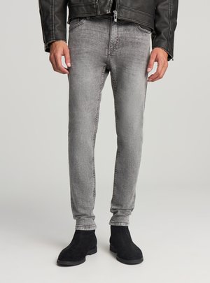 Jeans in denim grigio a taglio slim, caratterizzati da una texture sbiadita e dettagli di cucitura, abbinati a stivaletti alla caviglia in suede nero.