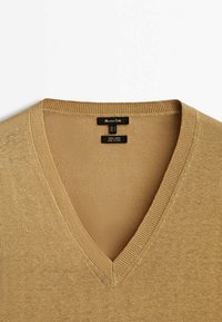 Pull beige en lin à col en V avec détail en maille côtelée au col et étiquette de marque indiquant la taille moyenne et le matériau 100 % lin.