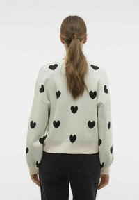 Sweat-shirt vert clair avec des motifs de cœurs noirs, des poignets côtelés, des épaules tombantes et une coupe décontractée. Texture douce.