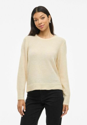 Pull en maille beige clair avec un col rond, des manches longues et une coupe légèrement cropped. Texture douce avec un ourlet et des poignets côtelés.