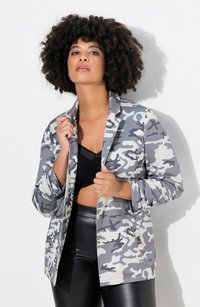 Blazer mimetico grigio leggero con una vestibilità rilassata, caratterizzato da rever a punta e maniche a cilindro, indossato sopra una maglia nera e pantaloni.