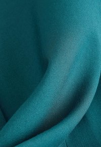 Tissu turquoise lisse avec une texture de tissage diagonal fin, délicatement plié pour montrer un drapé doux et des reflets subtils de lumière.
