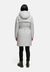 Grå, polstret frakke med hætte og bælte i taljen. Har en glat tekstur og et enkelt design. Sorte bukser og støvler bæres nedenunder.