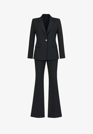 Completo da donna nero con blazer a un bottone dorato e pantaloni svasati, caratterizzato da rever e tasche con pattina frontali sul blazer.