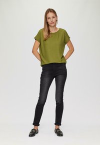 Groene, gestructureerde, korte mouwen top in combinatie met slim-fit zwarte jeans en zwarte loafers. De jeans zijn aan de enkels omgeslagen.
