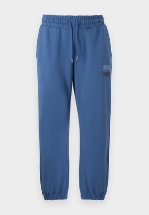 Pantalon de jogging bleu en matériau doux, doté d'une taille élastique, d'un cordon de serrage et de poignets élastiques. Comprend un écusson logo sur la cuisse.
