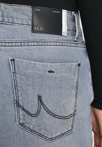 Ανοιχτό μπλε τζιν παντελόνι με πίσω τσέπη, μαύρη ραφή και μαύρη δερμάτινη ετικέτα μάρκας πάνω από την τσέπη.