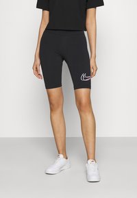 Svarta cykelshorts gjorda av elastiskt tyg, med en flerfärgad Nike-logotyp på låret. Kombinerat med en svart kortärmad t-shirt och vita sneakers.