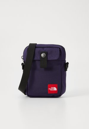 Saco de ombro em nylon roxo com aba frontal, fecho de botão de pressão, alça preta ajustável e um patch de logotipo vermelho na frente.