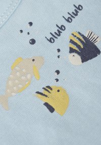 Ljusblått tyg med broderade fiskdesigns i gult och svart, med bubblor och texten 'blub blub' ovanför, vilket skapar ett lekfullt tema.