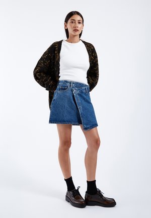 Farkkuhame, jossa on kietaisumalli, yhdistettynä valkoiseen tiukkaan toppiin ja mustaan kuvioituun neulecardiganiin. Mustat kengät paksulla pohjalla ja sukat.