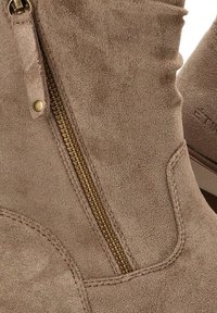 Botas de ante taupe hasta el tobillo con un detalle de cremallera dorada. Presentan costuras cosidas y una textura suave, resaltando el material blando.