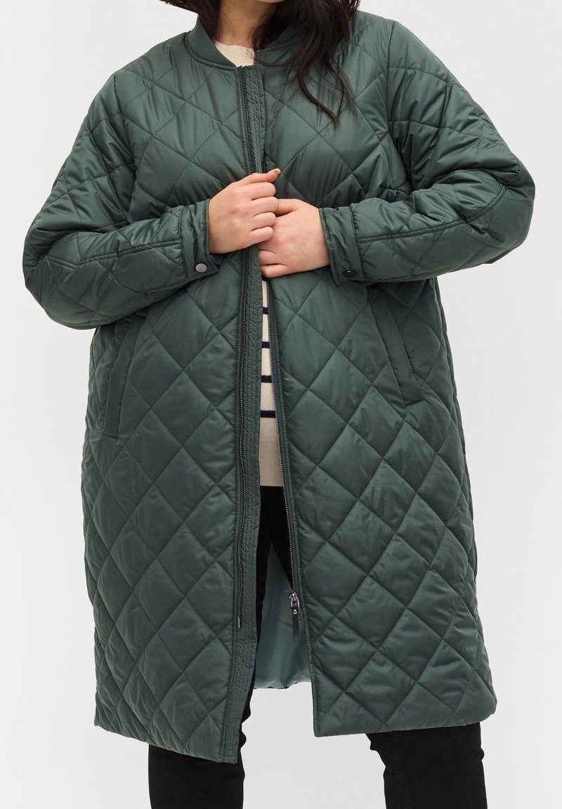 Gequilted groene jas met een ronde kraag, een ritssluiting aan de voorkant en twee zijzakken. Zachte, gladde textuur met een ruitpatroon.