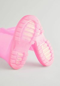 Stivali di gomma rosa traslucidi con suole testurizzate dotate di scanalature e sporgenze per una migliore aderenza; finitura lucida sulla superficie esterna.