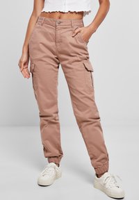 Světle růžové cargo kalhoty vyrobené z bavlny, s bočními kapsami, elastickým pasem a elastickými manžetami. Kombinované s bílými teniskami.