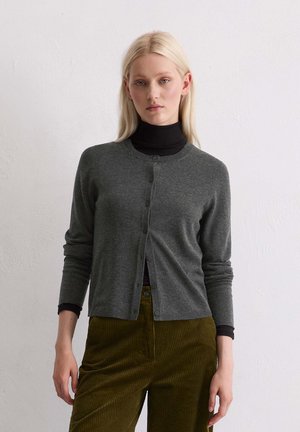 Grauer Cardigan aus feinem Strickmaterial mit rundem Ausschnitt, Knöpfen vorne und langen Ärmeln, getragen über einem schwarzen Rollkragenpullover und Cordhosen.