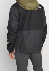 Chaqueta de hombre con un cuerpo negro y capucha verde oliva, fabricada en material ligero, con puños elásticos y un corte holgado.