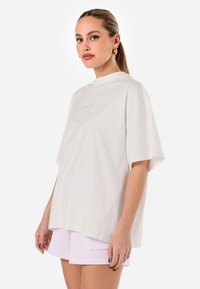 White oversized t-shirt with a high neckline and short sleeves, featuring subtle logo embroidery. Paired with light pink ribbed shorts.