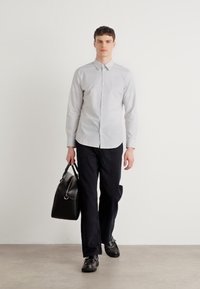 Camisa de rayas finas en gris claro con un cuello clásico, combinada con pantalones oscuros y zapatos negros, sosteniendo un bolso de cuero negro.