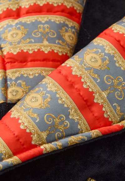 Kviltna tkanina z rdečimi in zlatimi vzorci na sivi podlagi; vsebuje zapletene oblikovne vzorce z bogatimi detajli in kontrastnimi teksturami.