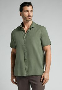 Camisa de manga corta con cuello en un tejido verde suave con una textura sutil, que presenta un cierre frontal de botones y un corte relajado.