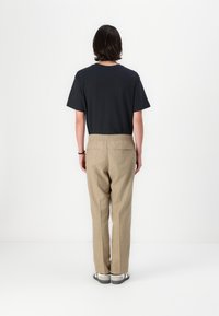 Camiseta negra de manga corta, corte relajado, combinada con pantalones beige de cintura elástica. Diseño simple, sin patrones ni acentos visibles.