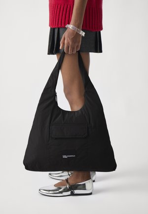 Black nylon oversized tote bag with a rounded shape, zippered pocket, and logo patch. Smooth texture and wide shoulder strap for carrying.