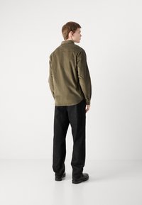 Olive green shirt with a buttoned collar, long sleeves, and a relaxed fit, paired with dark textured pants and black shoes.