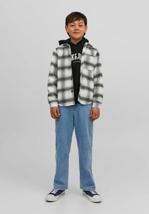 Camisa de franela a cuadros en blanco y negro sobre una sudadera negra, combinada con jeans de color azul claro y zapatillas negras con suelas blancas.