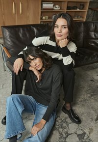 Deux personnes en tenue décontractée : l'une porte une chemise à rayures noires et blanches, l'autre un pull sombre associé à un jean bleu large.