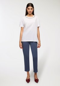 Biała koszulka z krótkim rękawem ozdobionym kołnierzykiem, zestawiona z dopasowanymi ciemnoniebieskimi spodniami i burgundowymi płaskimi butami w szpic. Gładkie tekstury na całej powierzchni.