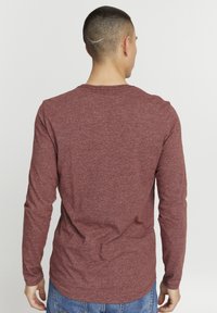 Langermet skjorte i mørkerød, laget av et strukturert stoff, med rund hals og en avslappet passform, kombinert med blå jeans.