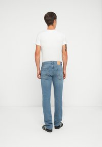 Jeans de mezclilla azul con corte recto, cinco bolsillos y un parche de cuero marrón en la parte trasera de la cintura. Combinados con una camiseta blanca básica.