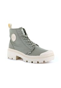 Zapatilla alta de lona verde claro con puntera de goma, suela gruesa de color crema, ojales de metal y un parche redondo en el costado.