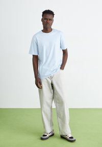 Light blue cotton T-shirt with crew neckline, paired with oversized light gray denim jeans. Black and pink sneakers complete the outfit.