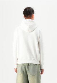 Felpa bianca con cappuccio e polsini e orlo a costine, abbinata a pantaloni in denim verde sbiadito. Il tessuto sembra morbido e informale.