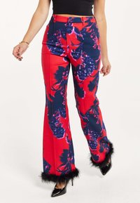 Flared trousers in a bold red fabric with a floral print in navy and pink, featuring black fur accents at the hems and a high-waisted design.