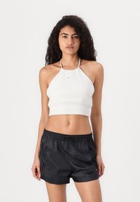 Svijetlosivi halter crop top s elastičnom trakom i malim logotipom, uparen s crnim najlonskim sportskim šortsevima koji imaju elastičnu traku u struku.