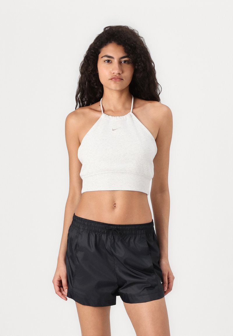 Svijetlosivi halter crop top s elastičnom trakom i malim logotipom, uparen s crnim najlonskim sportskim šortsevima koji imaju elastičnu traku u struku.