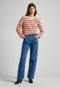 Maglione a righe rosse e crema con scollatura ampia, abbinato a jeans in denim blu a vita alta. Modella che indossa stivali neri con tacco.