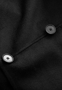 Tissu en laine noire à la texture douce, présentant deux boutons ronds en plastique noir avec un design à quatre trous, posés sur une surface lisse.