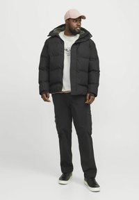 Zwarte pouchejacket met capuchon, grijze binnenkant, een witte grafische sweatshirt, zwarte cargobroek en zwarte sneakers. Zachte textuur overal.