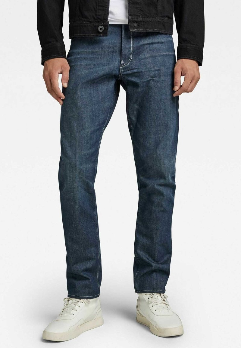 Granatowe jeansy z denimu o prostym kroju, z kontrastującymi przeszyciami i gładką fakturą, w zestawieniu z białymi trampeczkami.