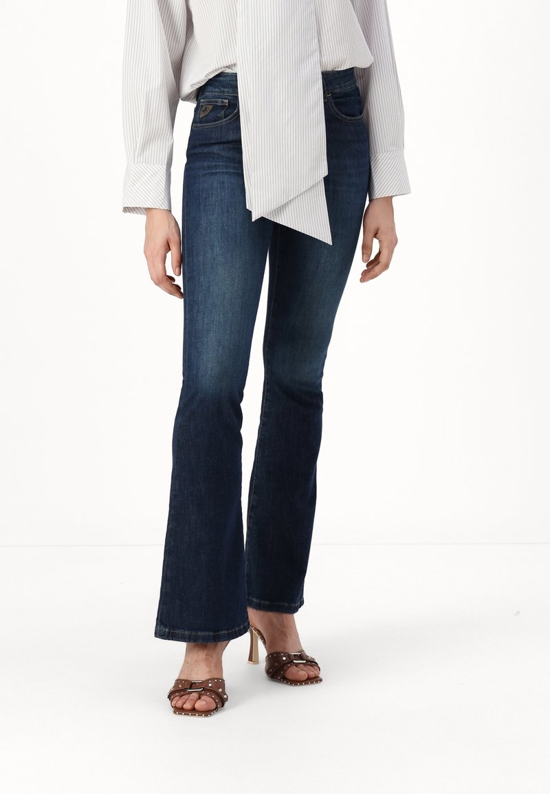 Mörk tvättade utsvängda jeans med en åtsittande midja, subtila sömdetaljer och ett medeltungt jeanstyg. Bruna klacksandaler fulländar looken.