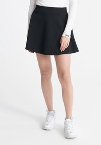 Zwarte rok met een gegolfd zigzagpatroon, uitdijend ontwerp, lengte tot halverwege de dij, gecombineerd met witte sportschoenen.