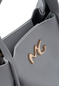 Borsa sintetica grigia con texture liscia, forma strutturata e un prominente accento dorato del logo sulla parte anteriore.