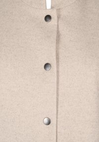 Giacca in feltro beige con colletto rotondo, chiusura frontale con bottoni metallici argentati e superficie liscia e strutturata.