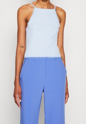 Light blue ribbed tank top with scalloped edges, paired with high-waisted blue trousers. Top has a fitted shape and thin straps.