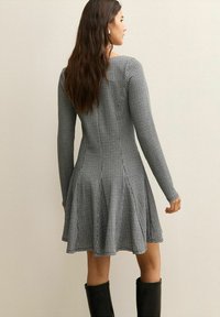 Zwart-wit geruit jurkje met lange mouwen, aansluitende top, uitlopende rok en een gladde textuur, gedragen met zwarte laarzen tot op de knie.