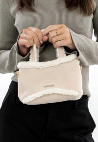 Beige handbag with fluffy white trim, rectangular shape, short handles, smooth texture, and a gold logo on the front.